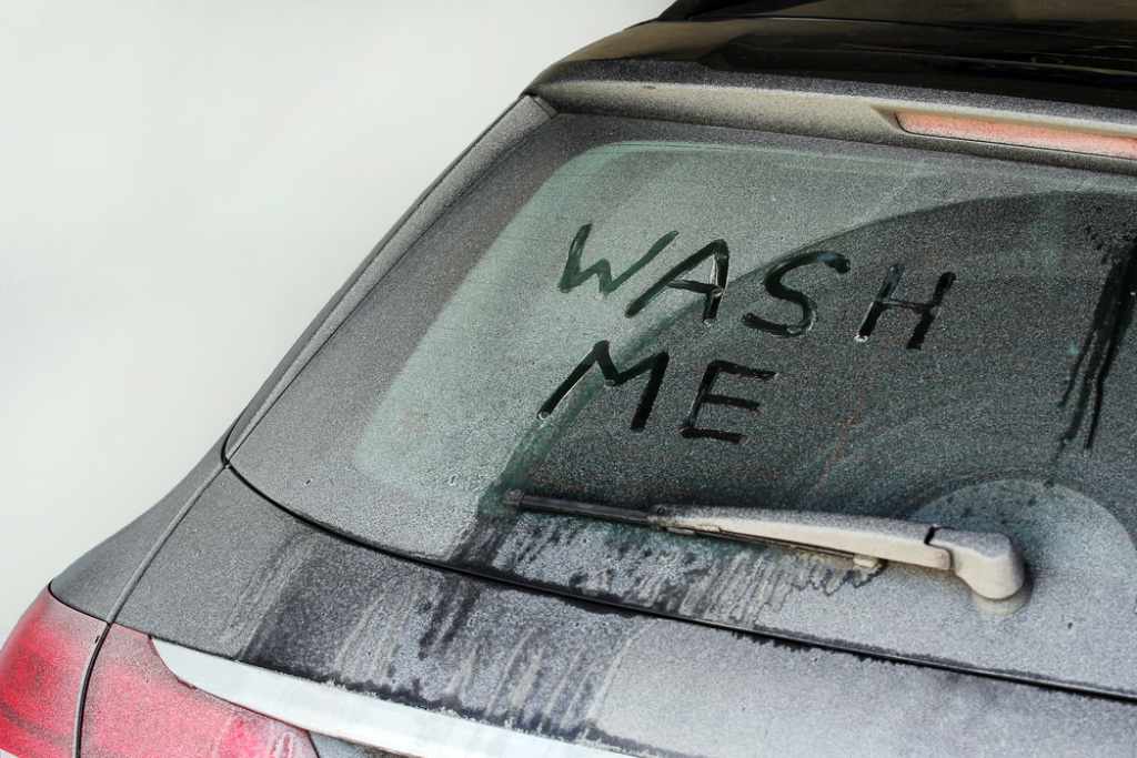 A dirty car windshield that says “Wash Me”