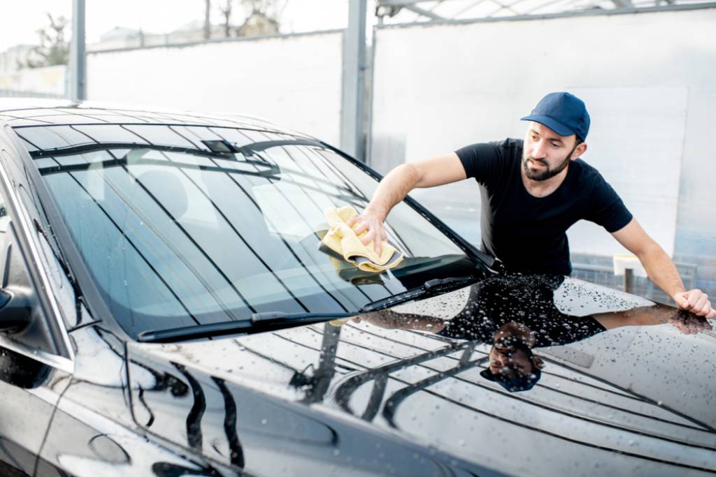 A man washing a car’s windshield with a cloth