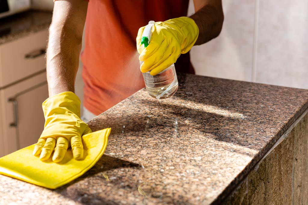 Someone cleaning a granite countertop with a spray bottle and a cloth