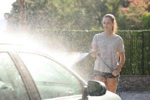 A young woman spraying a car with a hose.
